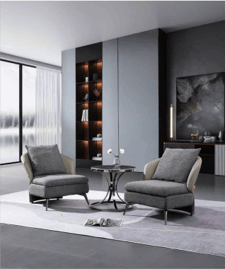 A modern living room with two gray armchairs facing a small round table. Behind is a tall shelf with warm lights, abstract art, and a large window.