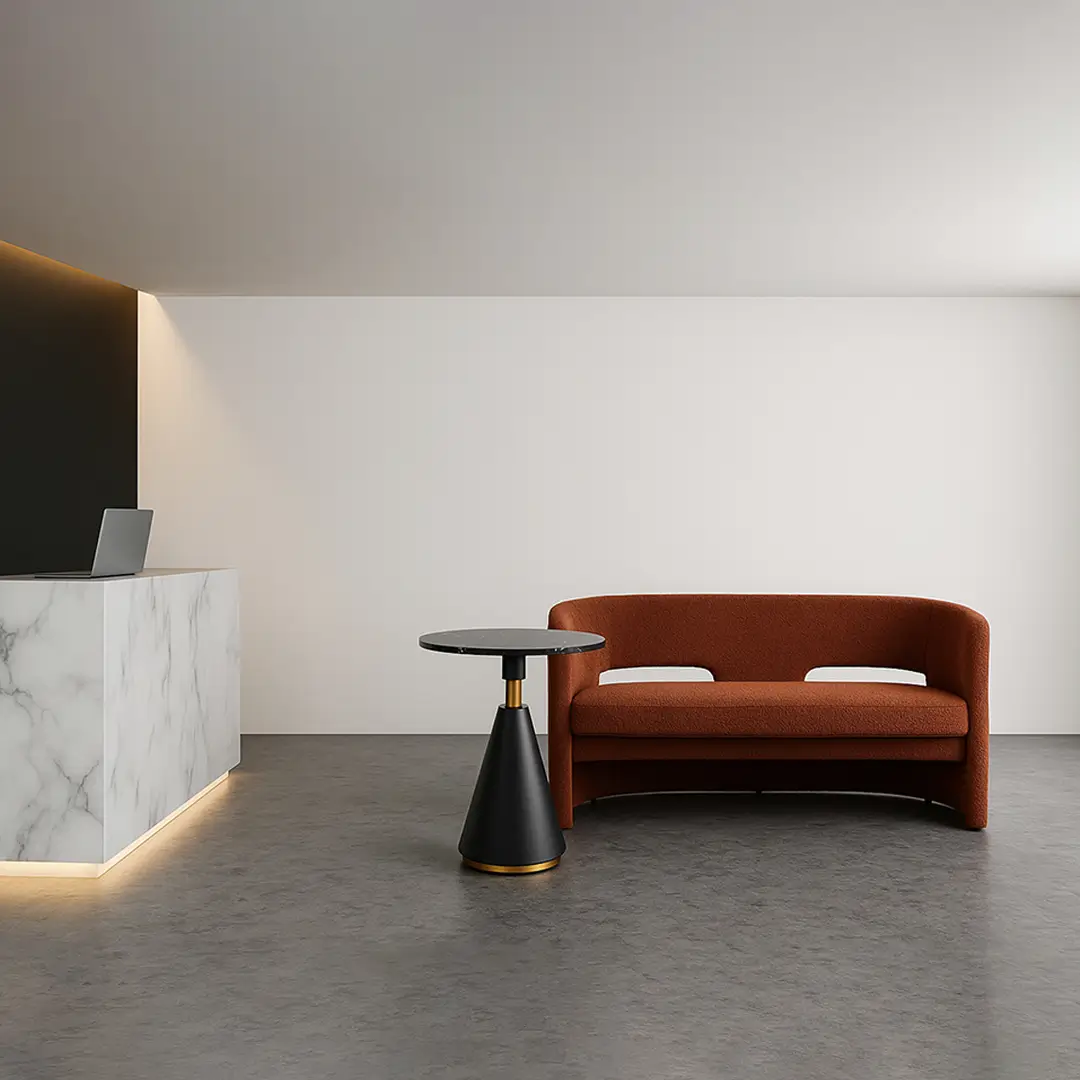 Modern interior with a sleek marble reception desk on the left, a round black side table, and a rust-colored sofa on the right. Minimalist and calm.