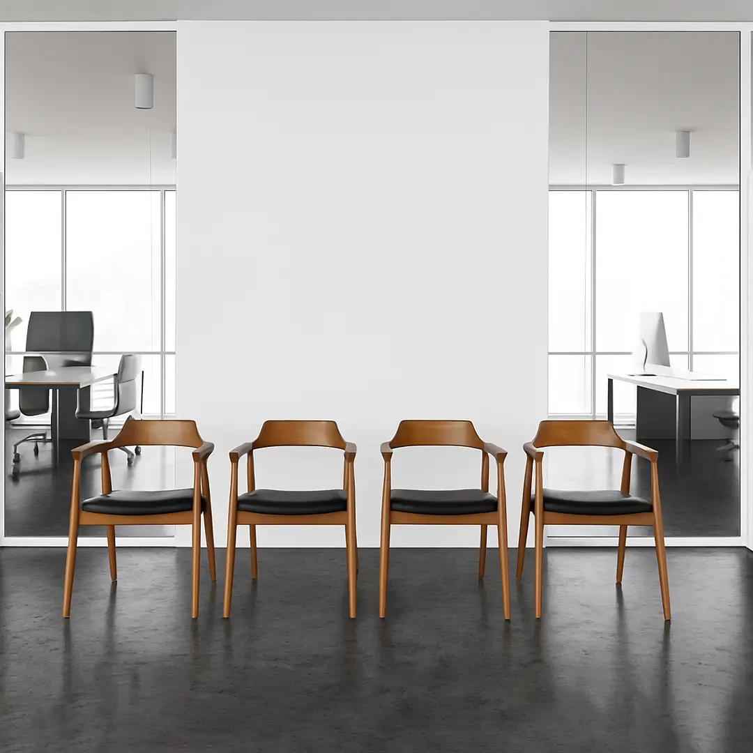 Four wooden chairs with black cushions are lined against a white wall in an office lobby. Glass windows reveal two modern desks in adjacent rooms.