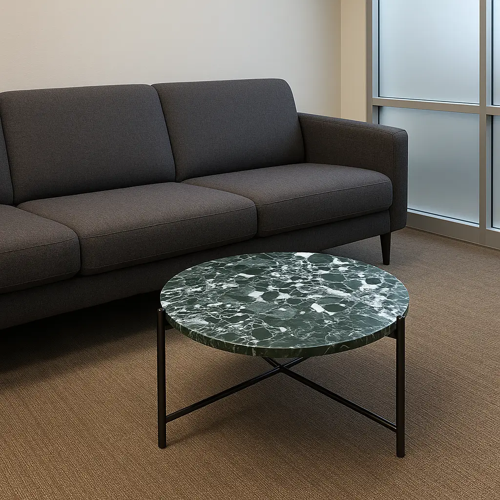A modern living room with a dark gray couch and a round green marble coffee table on a beige carpet. Large frosted window in the background.