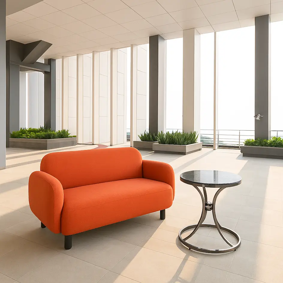 Modern rooftop lounge with an orange sofa and circular black table. Surrounded by tall windows, gray columns, and green plants. Bright and airy ambiance.