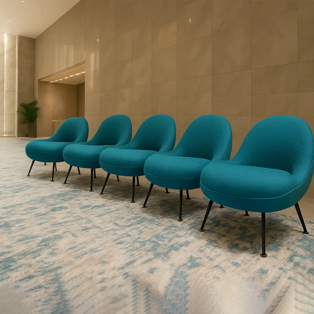 Five modern teal chairs lined up on a patterned carpet in a minimalist lobby with beige walls. The atmosphere is calm and sophisticated.