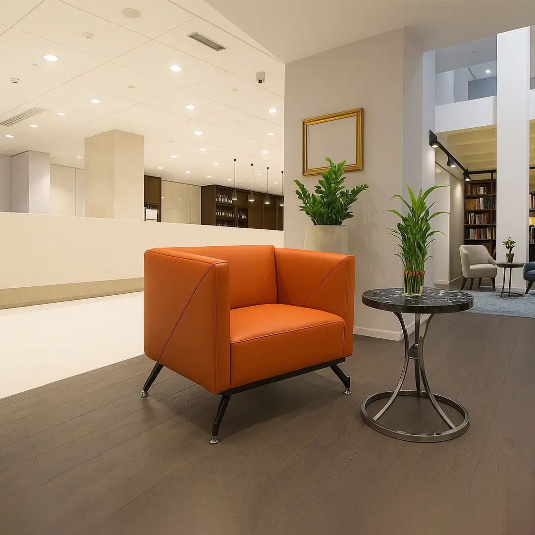 Modern lounge area with an orange armchair, round black table, and green potted plants. Soft lighting and wood flooring create a cozy ambiance.