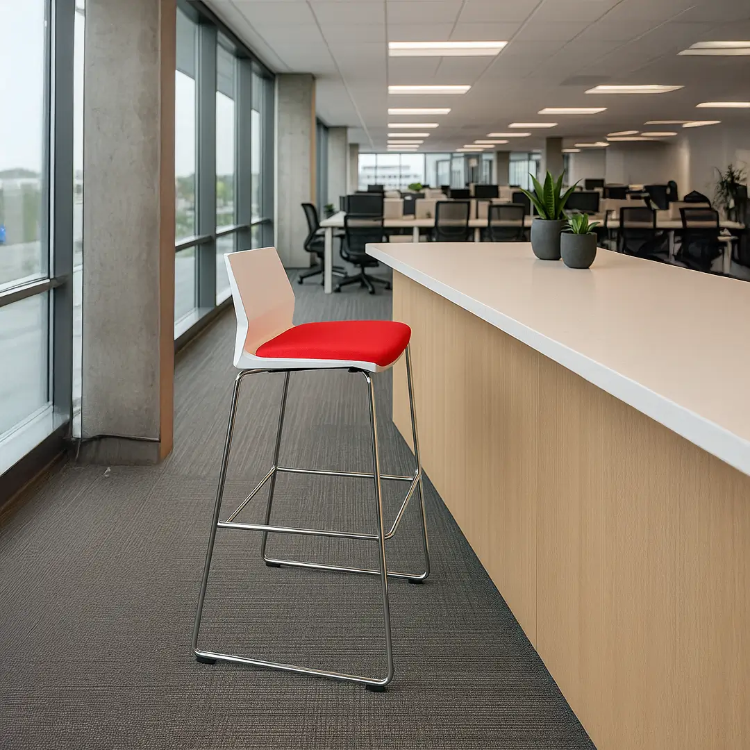 Modern office interior with large windows, a tall, light wood counter, and a red and white chair. Workstations with black chairs and plants in the background.