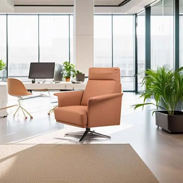 A modern office features a comfortable orange armchair on a light rug, with a sleek desk, computer, chair, and green plants in the sunny background.