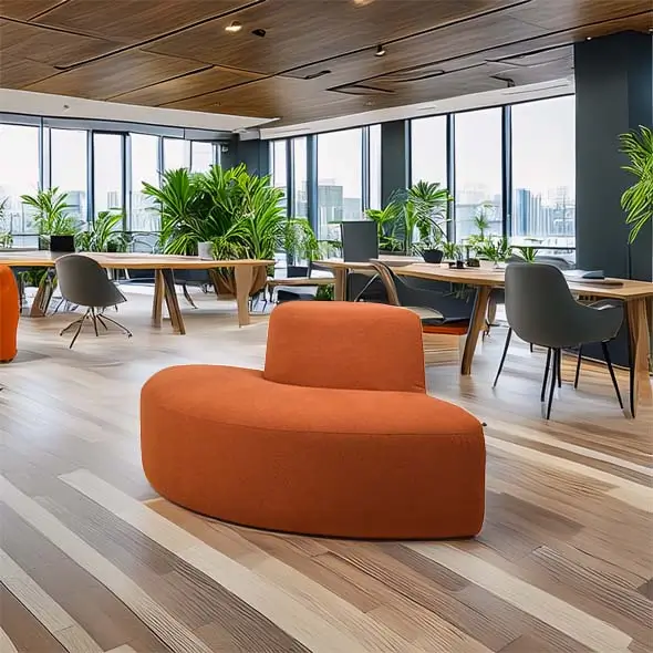 Spacious modern office with large windows, lush green plants, and wooden ceilings. Features a curved orange sofa and wood desks with gray chairs.