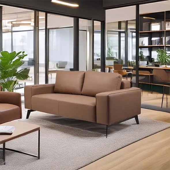 A modern office space with a brown leather sofa on a gray rug. Glass walls reveal desks, plants, and shelves, creating an inviting, professional atmosphere.