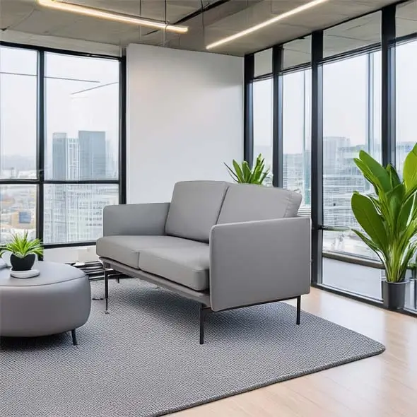Modern office lounge with a grey sofa and ottoman on a textured rug. Large windows offer a city view, and potted plants add a fresh touch.