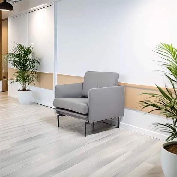 A modern office space featuring a gray armchair against a white wall, wooden paneling, and potted plants. The scene conveys a calm, minimalist vibe.