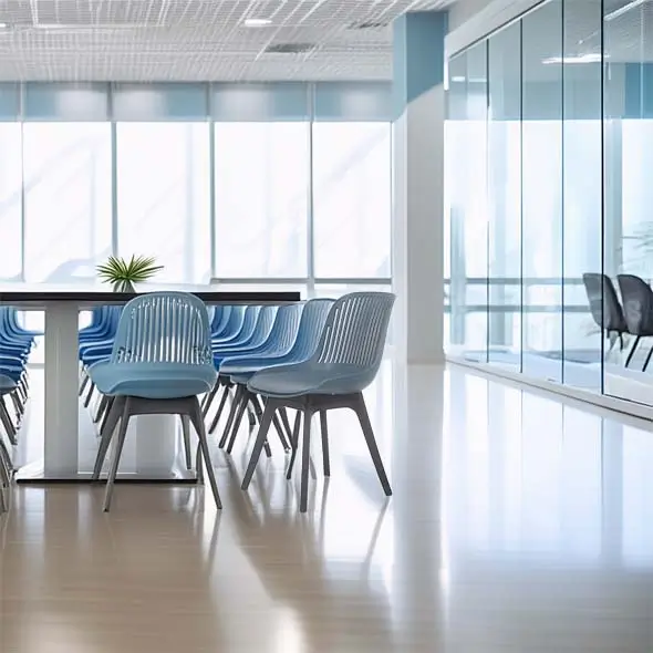 A modern conference room with blue chairs aligned along a long table. Large windows and glass walls fill the space with natural light, creating an open, airy atmosphere.