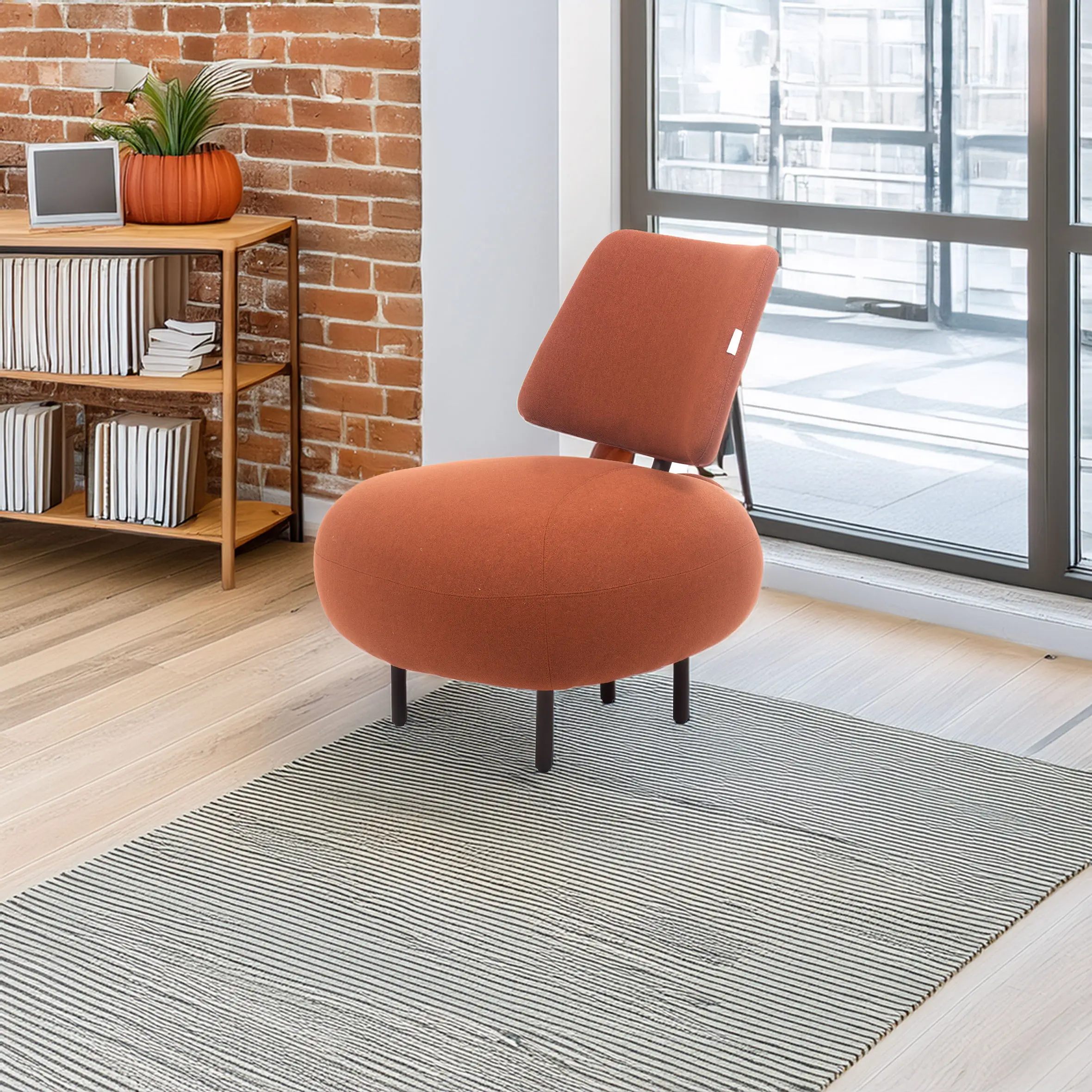 A modern room with a brick wall, featuring a round orange chair on a striped rug. A plant and books are on a shelf. Sunlight streams through a large window.