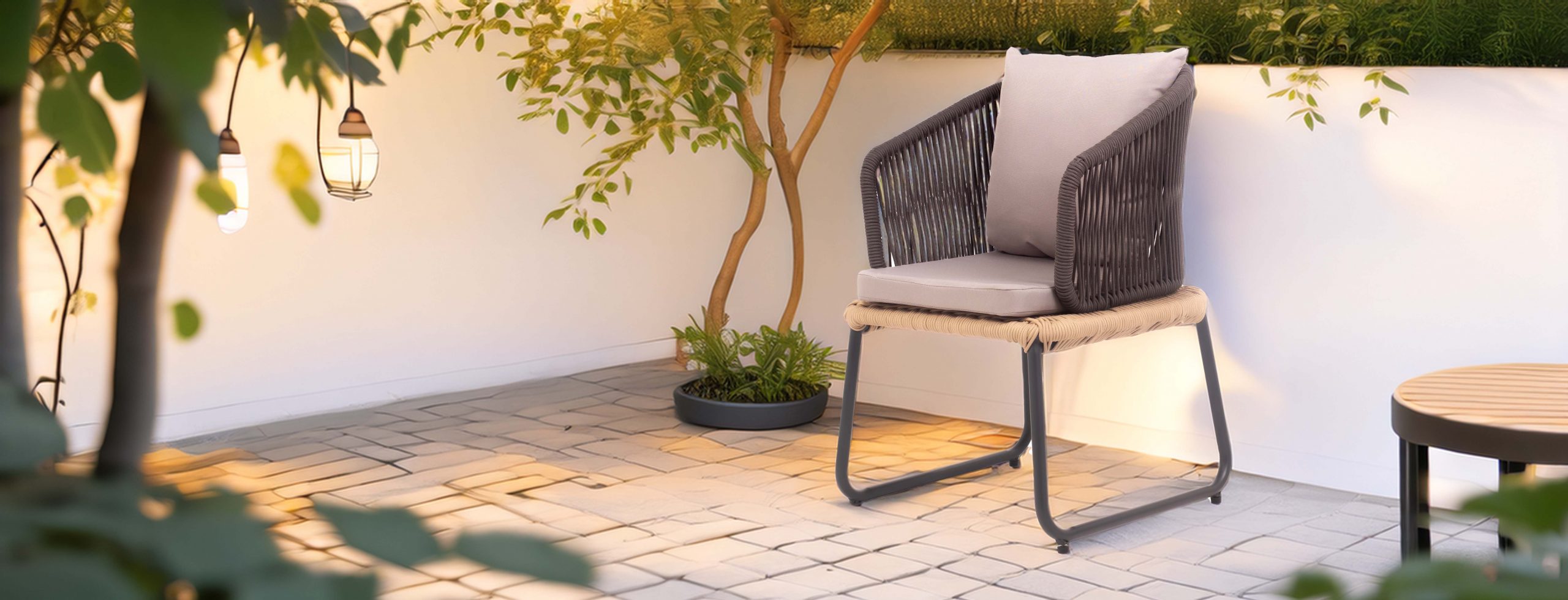 Outdoor patio with a wicker dining chair featuring gray cushions, beside a leafy potted plant against a white wall, creating a serene atmosphere.