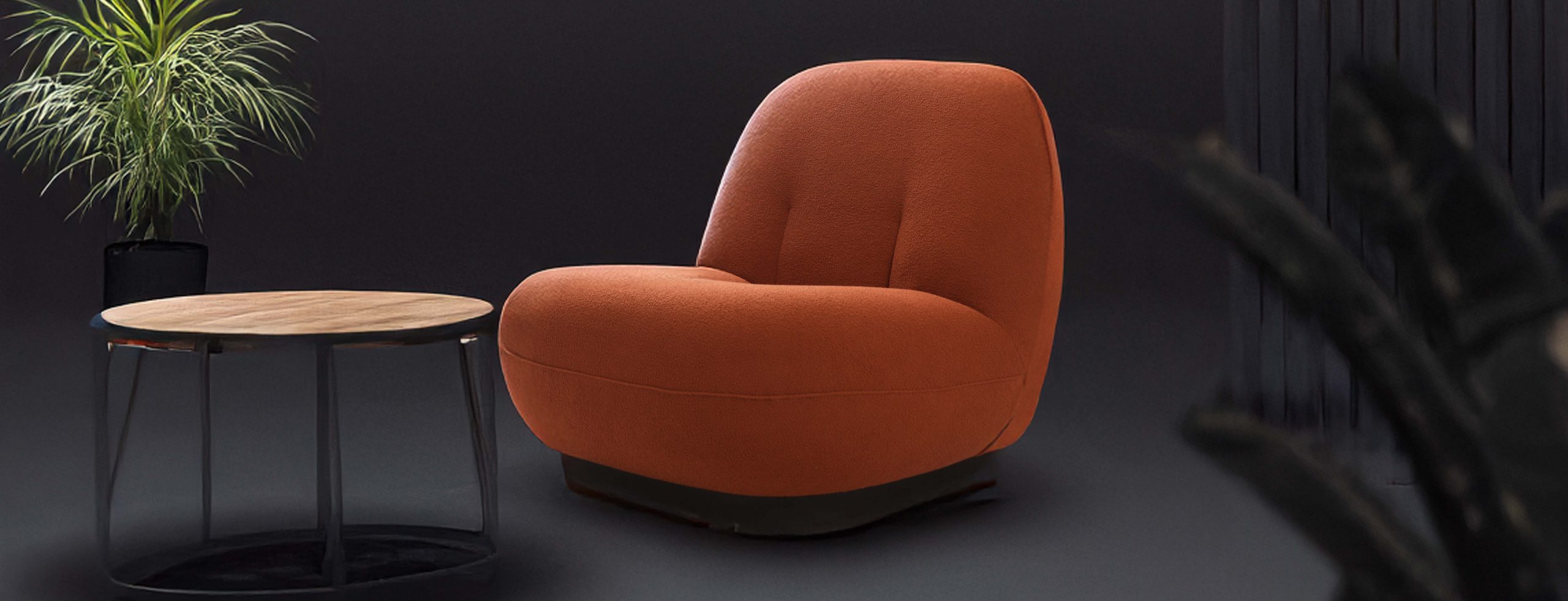 A cozy orange lounge chair against a dark background. A potted plant is nearby, adding a touch of greenery.
